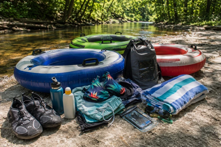 River tubing packing essentials beside colorful tubes and a wooded creek